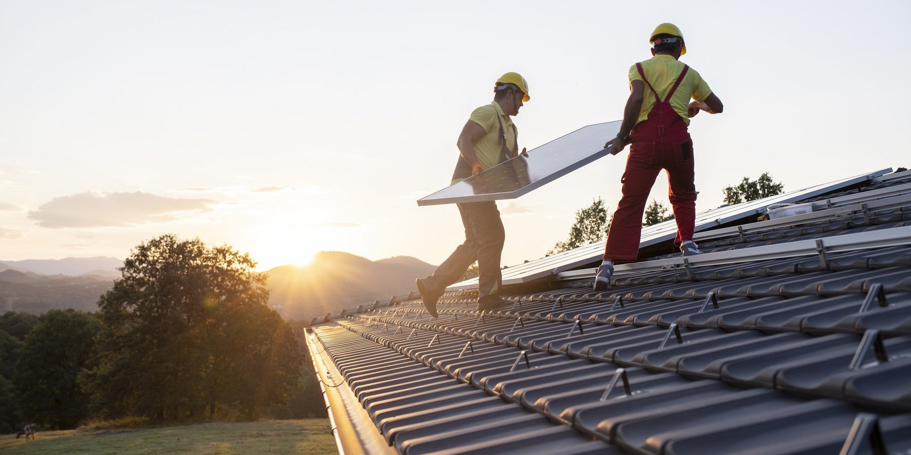 Zwei Arbeiter montieren ein Solarpanel auf dem Dach eines Eigenheimes.