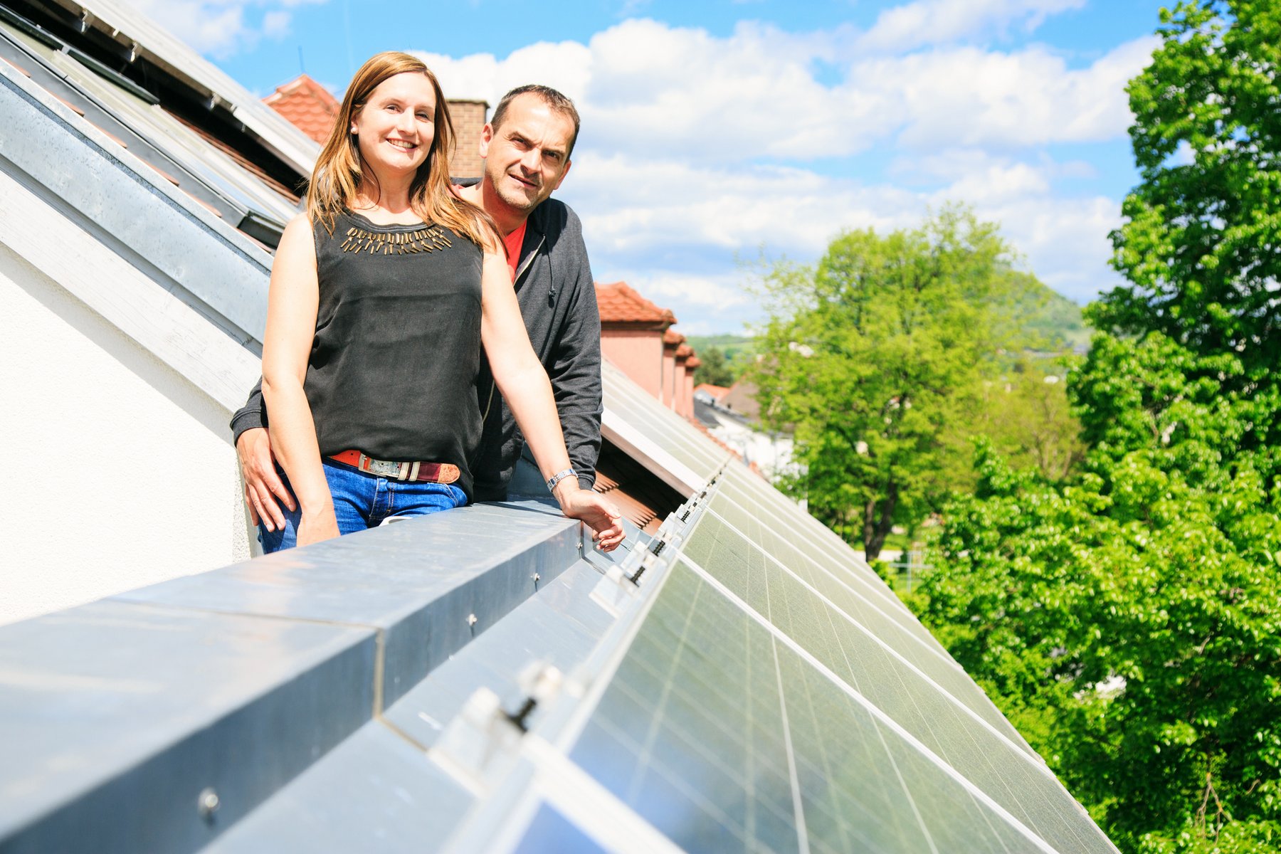 Eine Frau und ein Mann stehen auf einem Balkon. Unter dem Balkon erkennt man Solarpanels. Konzept der grünen Energie und der nachhaltigen Zukunft für die nächsten Generationen.